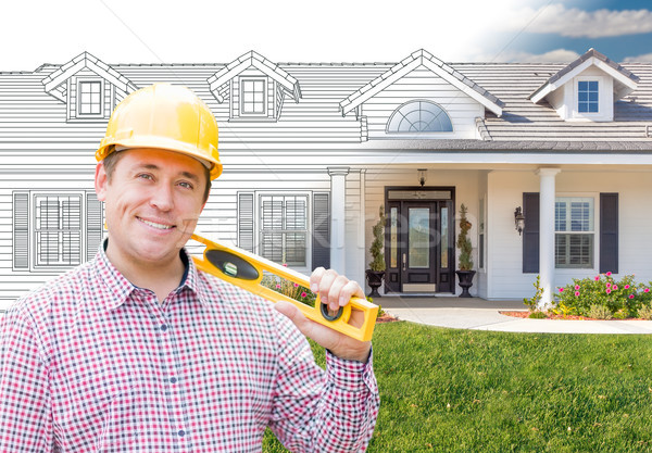 Male Contractor Wearing Hard Hat In Front Of House Drawing Grada