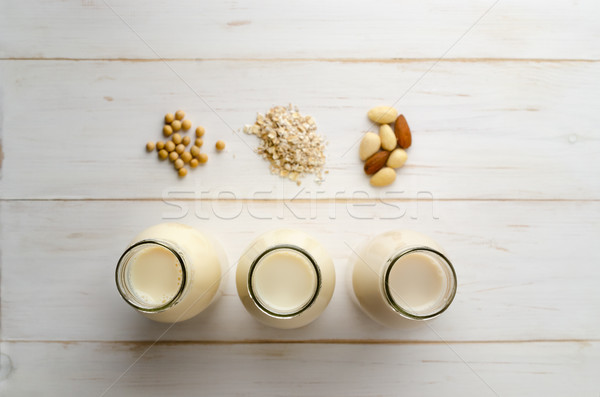 Row of Bottled Milk Substitutes with Ingredients on White Wood P Stock photo © frannyanne