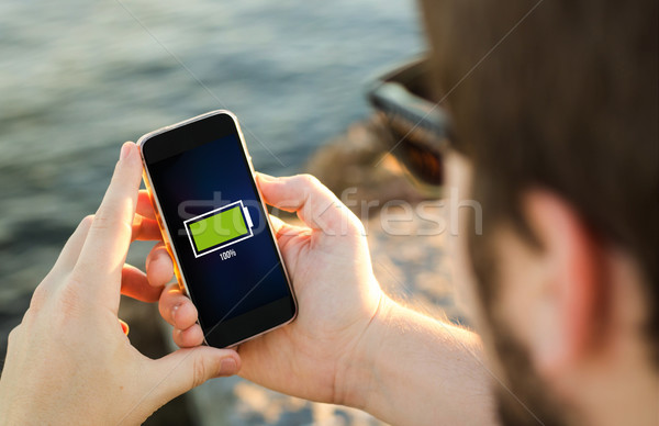 Stock photo: Man using his  mobile phone on the coast with full battery on th