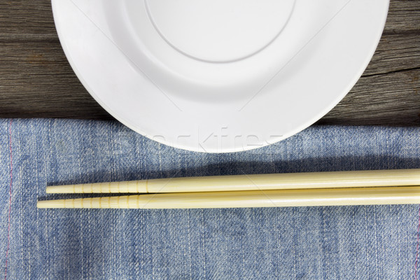 wood background plates, chopsticks and spoons on blue jeans text Stock photo © Gloszilla