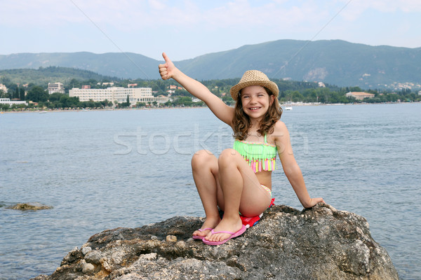 happy little girl with thumb up sitting on a rock by the sea Stock photo © goce