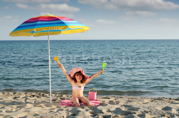 happy little girl with hands up sitting under sunshade on beach Stock photo © goce