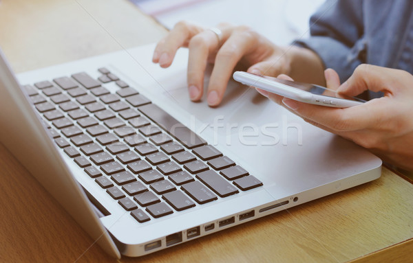 Woman's hands using smartphone and laptop in workplace or home Stock photo © happydancing