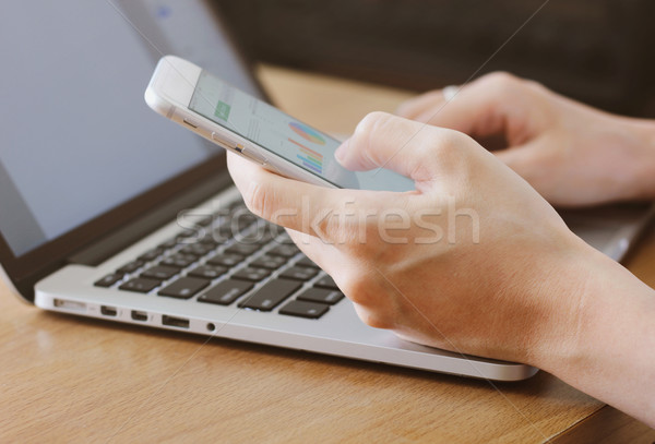 Hand using smartphone showing business graphs and typing laptop Stock photo © happydancing