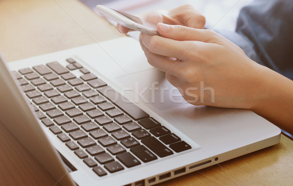 Woman's hands using smartphone and laptop in workplace or home Stock photo © happydancing