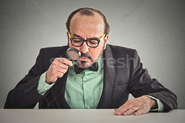  man sitting at desk skeptically looking through magnifying glass Stock photo © ichiosea