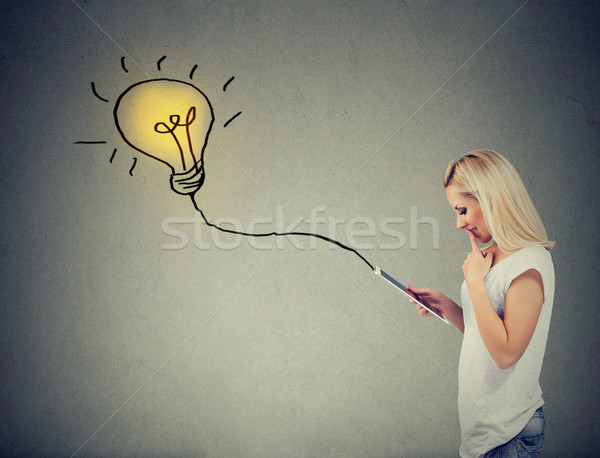 Thoughtful woman using a tablet computer with light bulb plugged in it Stock photo © ichiosea