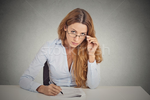Stock photo: businesswoman with glasses sitting at desk skeptically looking at you scrutinizing