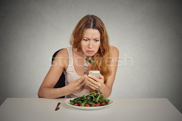 Displeased girl eating green salad looking at phone seeing bad news  Stock photo © ichiosea