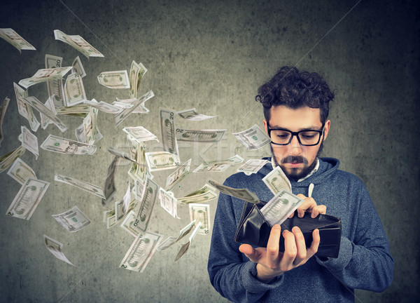 Hipster man looking at his wallet with money dollar banknotes flying out away  Stock photo © ichiosea