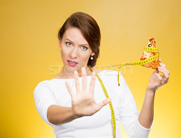 Stock photo: woman saying no to fatty pizza with measuring tape around, trying to resist temptation to eat it