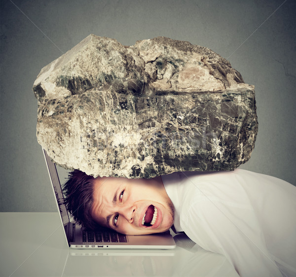 Desperate business man with head squeezed between laptop and rock Stock photo © ichiosea