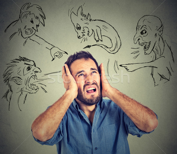 Stressed young man covers his ears with his hands evil guys pointing fingers at him Stock photo © ichiosea