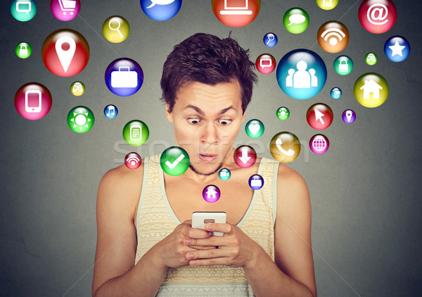 Shocked man using smartphone application icons flying out of cellphone Stock photo © ichiosea