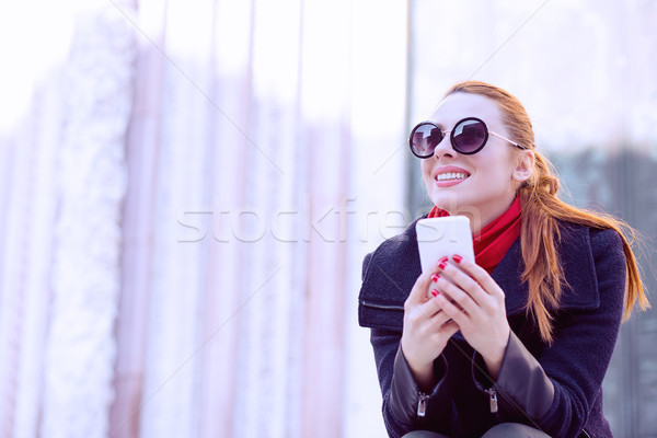 Beautiful woman sitting at the street holding her mobile phone smiling  Stock photo © ichiosea