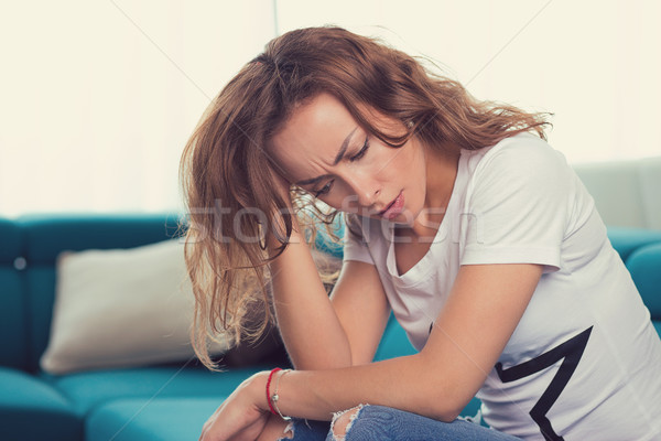 Stock photo: sad woman with a hand on the head sitting on a couch in the living room at home 