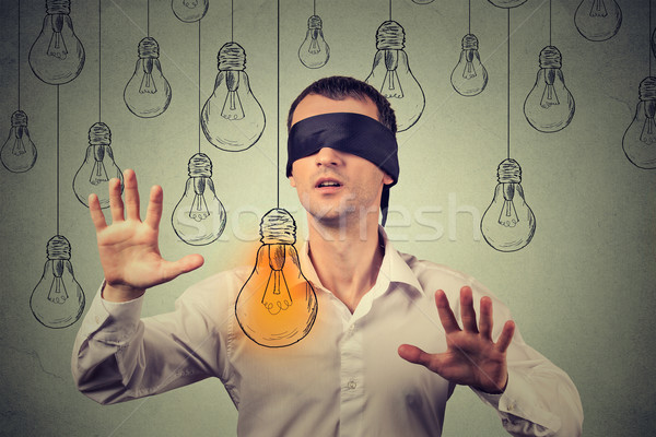 Blindfolded young man walking through light bulbs searching for bright idea Stock photo © ichiosea