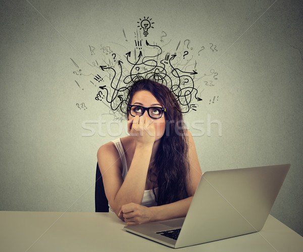 woman with thoughtful expression sitting at a desk with laptop with arrows and symbols coming out of Stock photo © ichiosea