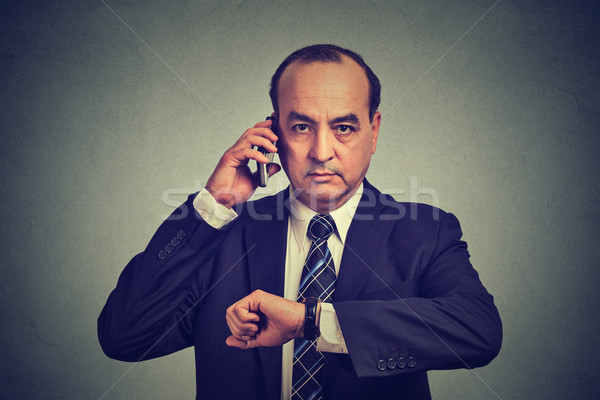 Business man looking at wrist watch, talking on mobile phone running late for meeting. Time is money Stock photo © ichiosea
