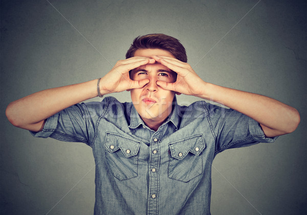 Displeased young man looking through fingers like binoculars Stock photo © ichiosea