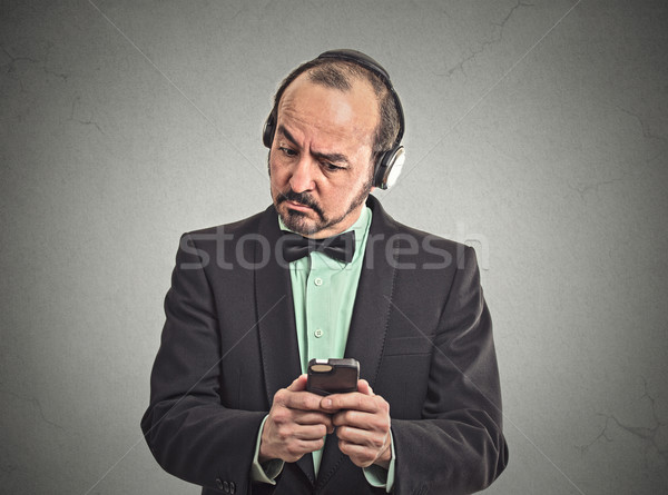 Confused man listening music with pair of headphones looking at his smartphone Stock photo © ichiosea