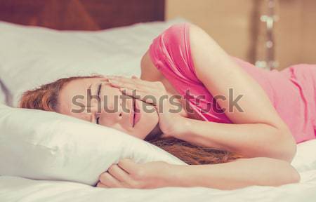 Sad woman lying in bed with her arms on head and eyes closed having headache  Stock photo © ichiosea