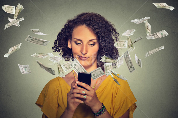 Annoyed young woman using smartphone with dollar bills flying away Stock photo © ichiosea