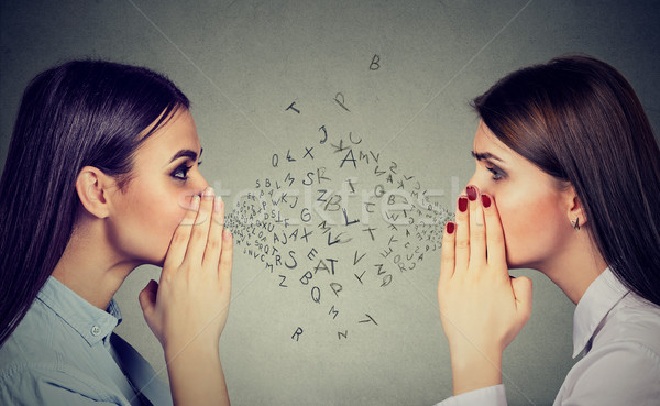 Two women whispering a gossip secret to each other with alphabet letters in-between Stock photo © ichiosea