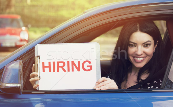 Stock photo: Happy woman sitting inside car showing white card with hiring sign message 