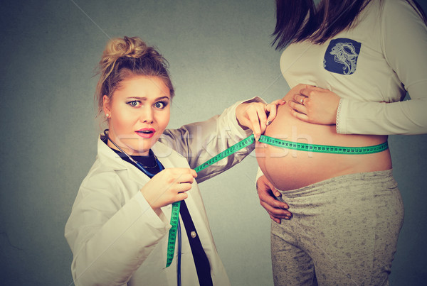 Pregnant woman exposing belly while a shocked gynecologist doctor uses measuring tape to follow grow Stock photo © ichiosea