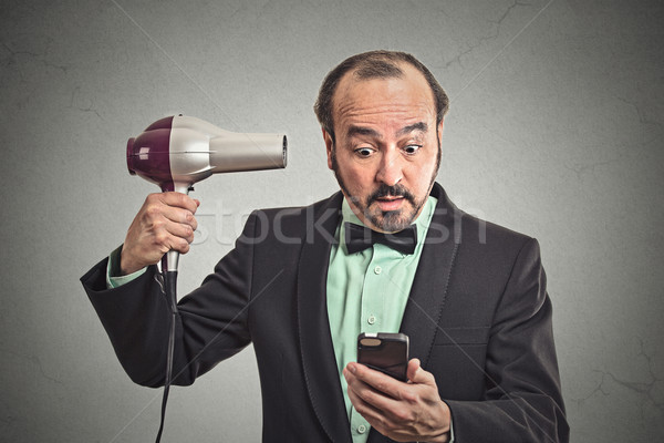 business man reading news on smartphone holding hairdryer Stock photo © ichiosea