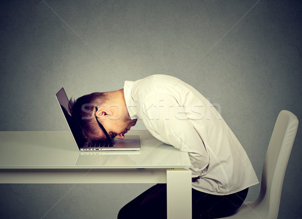 Stock photo: Desperate employee stressed young man resting head on laptop keyboard 