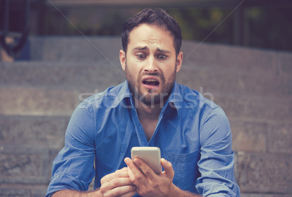 Stock photo: Anxious upset scared man looking at phone seeing bad news 