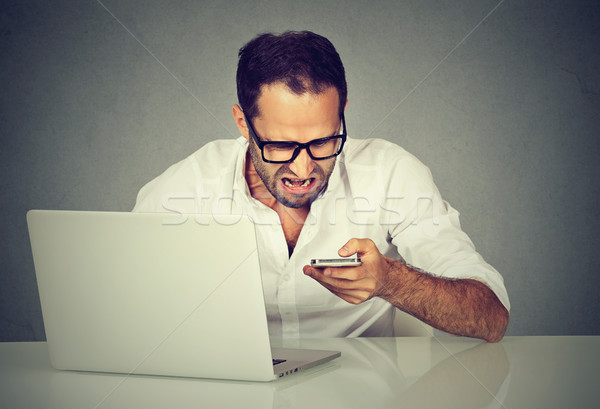 Frustrated man with laptop texting on his mobile phone  Stock photo © ichiosea