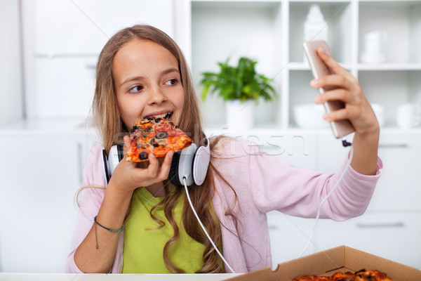 Young teenager girl eating pizza in the kitchen - making a selfi Stock photo © ilona75