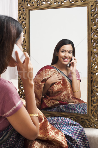 Reflection of a woman in mirror trying a sari on herself and talking on a mobile phone Stock photo © imagedb