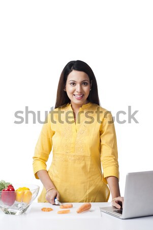 Stock photo: Woman using a laptop while cutting vegetables in a kitchen