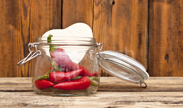 red chilly peppers in glass jar with cardboard heart on wood bac Stock photo © inxti