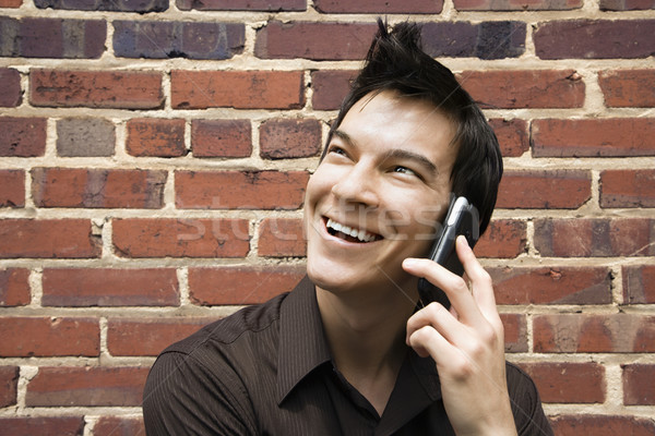 Homem celular sorridente jovem asiático parede de tijolos Foto stock © iofoto