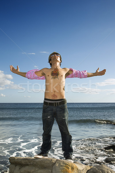 Young Man Standing on Ocean Rock with Arms Outstretched Stock photo © iofoto