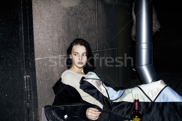 Stock photo: young poor ttenage girl sitting at dirty wall on floor with bottle of vine, poor refugee alcoholic, 