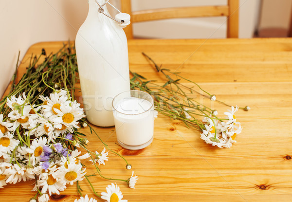 Simply stylish wooden kitchen with bottle of milk and glass on table, summer flowers camomile, healt Stock photo © iordani