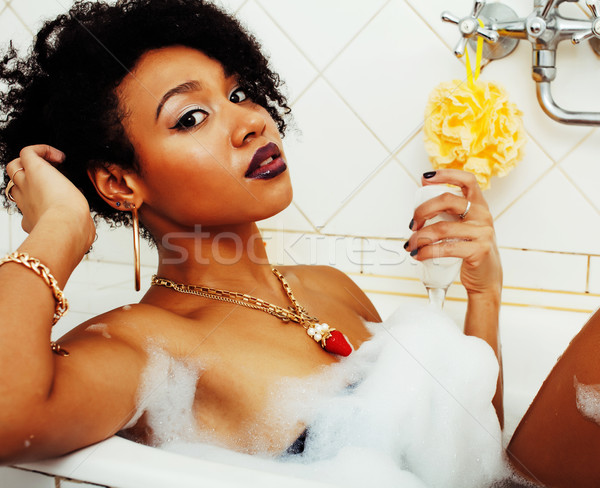 young afro-american teen girl laying in bath with foam, wearing swag jewelry flawless, making selfie Stock photo © iordani