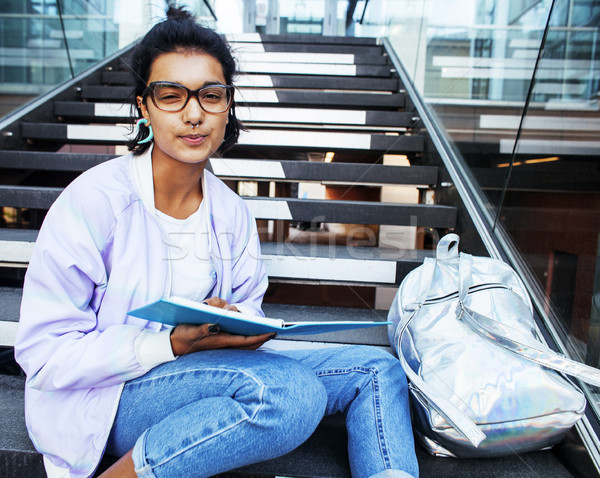 young cute indian girl at university building sitting on stairs reading a book, wearing hipster glas Stock photo © iordani