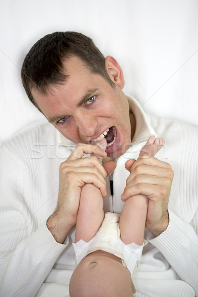 Young crazy father is loosing patience with baby and ready to bite her feet. Stock photo © iriana88w