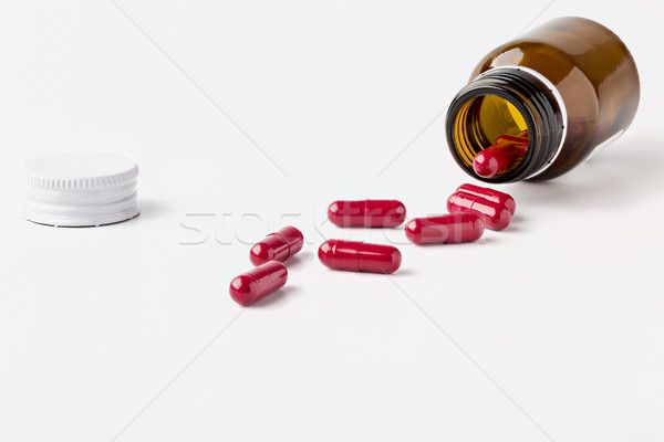 Open glass brown pill bottle and scattered red capsules Stock photo © ironstealth