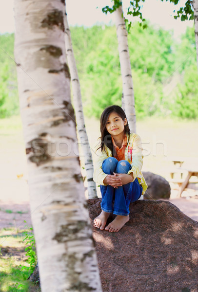 Young biracial girl sitting on rock under trees Stock photo © jarenwicklund