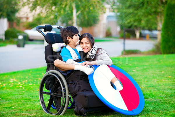 Disabled brother hugging older sister while sitting in wheelchair outdoors Stock photo © jarenwicklund
