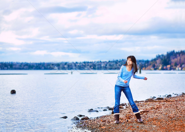 Stock photo: Teen girl throwing rocks in the water, along a rocky lake shore
