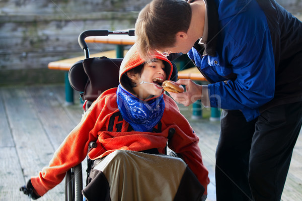 Father feeding disabled son a hamburger in wheelchair. Child has Stock photo © jarenwicklund